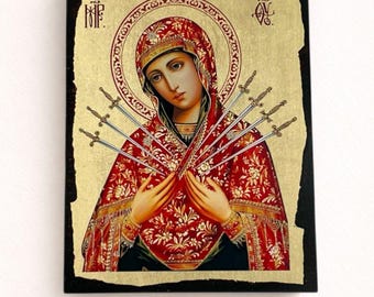 May include: A rectangular religious icon featuring a figure in a red floral head covering and garment, pierced by seven silver swords. The background is gold leaf with a black border, and the figure has a circular halo and Cyrillic text.