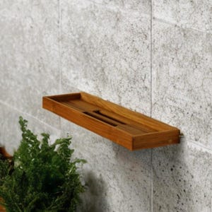 May include: A rectangular wall-mounted wooden shelf featuring a natural brown finish and a slatted base design. The shelf is constructed with four sides and is mounted horizontally against a light gray textured stone wall surface.