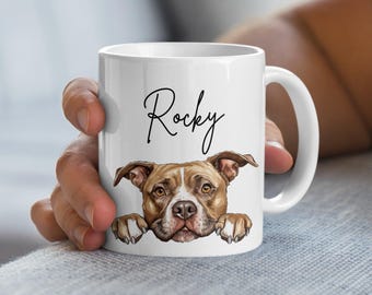 May include: White ceramic mug with a brown and white pit bull dog peeking over the rim. The dog's name, "Rocky", is written in black cursive on the mug.