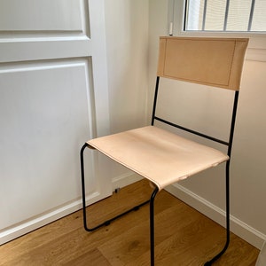 May include: A simple, modern chair with a black metal frame and a light brown leather seat and back.