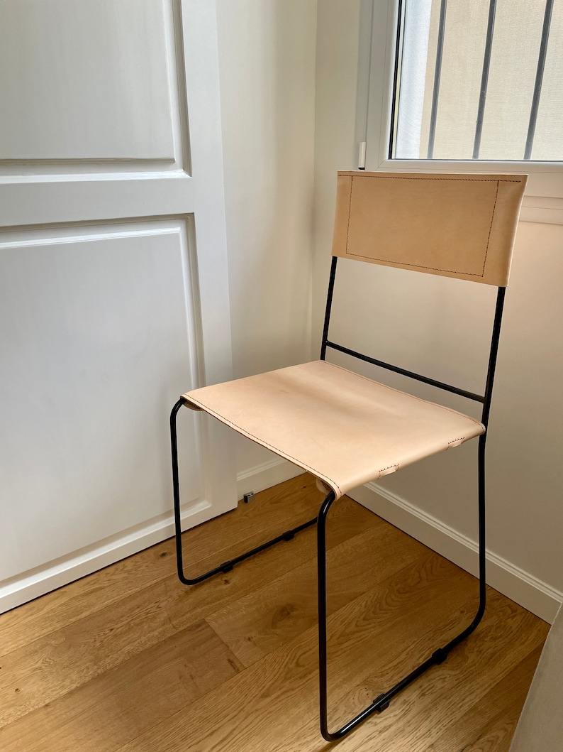May include: A simple, modern chair with a black metal frame and a light brown leather seat and back.