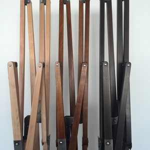 May include: Three wooden chair frames in different wood finishes: natural, oak, and walnut or wenge. The frames are made of wood and metal and are folded up.