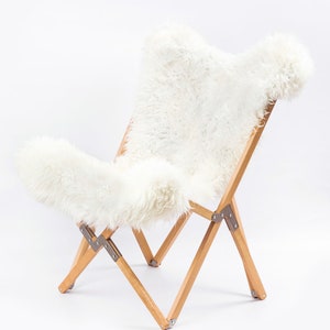 May include: A white sheepskin chair with a wooden frame. The chair is folded and has a white sheepskin seat and back.