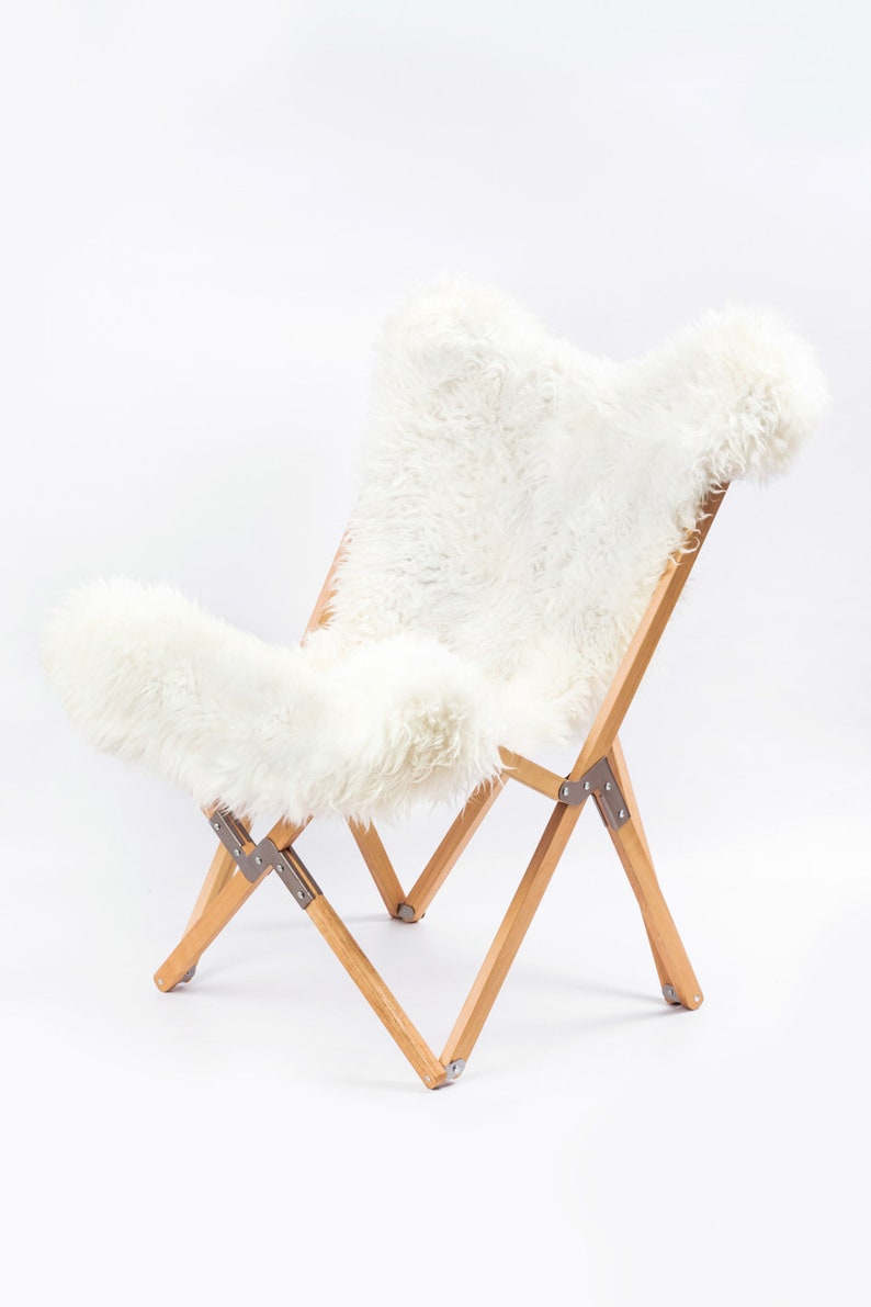 May include: A white sheepskin chair with a wooden frame. The chair is folded and has a white sheepskin seat and back.