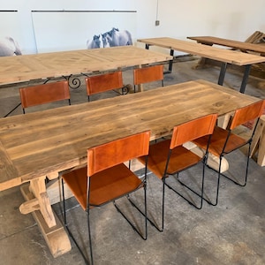 May include: A rustic wooden dining table with a distressed finish and a trestle base. The table is surrounded by six chairs with black metal frames and brown leather seats.