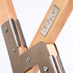 May include: Close-up of a wooden chair with metal joints. The chair has a metal plate with the text "BIGBKF1" on it.