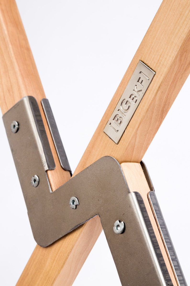 May include: Close-up of a wooden chair with metal joints. The chair has a metal plate with the text "BIGBKF1" on it.