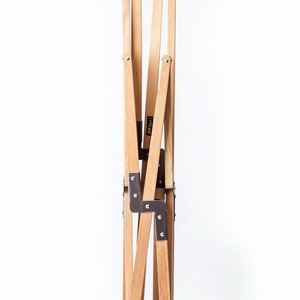 May include: A wooden folding chair with metal hinges. The chair is folded up and standing on a white surface.
