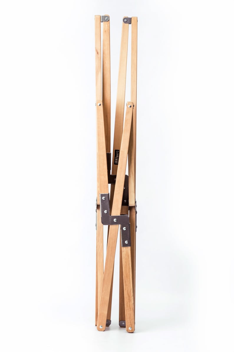 May include: A wooden folding chair with metal hinges. The chair is folded up and standing on a white surface.