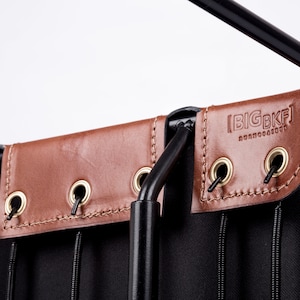 May include: Close-up of a black canvas bag with brown leather accents. The bag has a metal frame and a hanging loop. The leather accents have grommets and are stitched with a brown thread. The bag has the text "BIGBKF" embossed on the leather.