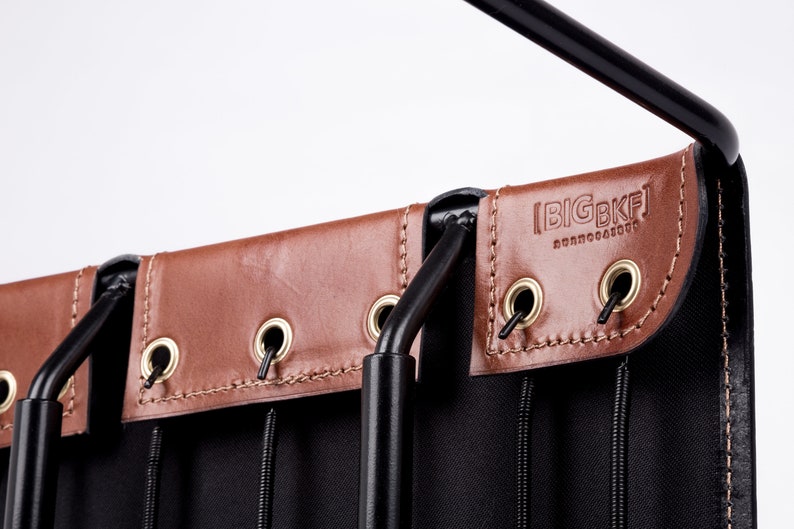 May include: Close-up of a black canvas bag with brown leather accents. The bag has a metal frame and a hanging loop. The leather accents have grommets and are stitched with a brown thread. The bag has the text "BIGBKF" embossed on the leather.