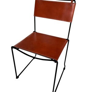 May include: A modern chair with a brown leather seat and backrest. The chair has a black metal frame with a minimalist design. The leather is stitched with white thread. The chair is suitable for indoor use.