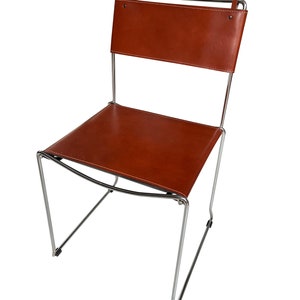 May include: A modern chair with a brown leather seat and backrest. The chair has a minimalist design with a chrome-colored metal frame. The leather is stitched with white thread. The chair is suitable for indoor use.