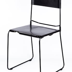 May include: Black leather chair with a metal frame. The chair has a simple design with a rectangular seat and backrest.