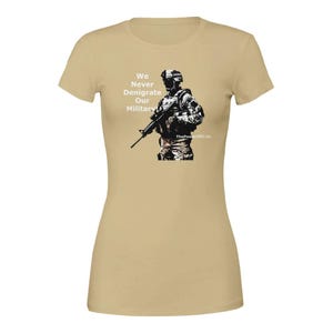 May include: A tan t-shirt with a graphic of a soldier holding a rifle. The text "We Never Denigrate Our Military" is printed on the shirt. ThePowerOfUs.co is printed at the bottom of the graphic.