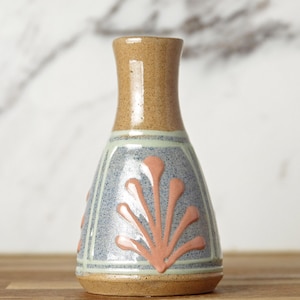 May include: A ceramic vase with a narrow neck and a wider base, featuring a speckled tan upper section and a lower body decorated with light blue panels, pale green borders, and raised peach-coloured fan-shaped floral motifs.