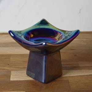 May include: An iridescent blue ceramic candle holder with a star-shaped top and a square base.