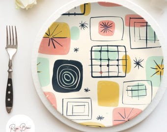 May include: A decorative plate with a mid-century modern design. The plate features a cream background with colorful geometric shapes in pink, yellow, teal, and navy blue. A fork and knife are on the right and left sides of the plate.