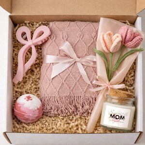 May include: A gift box containing a pink blanket, hair clip, bath bomb, crochet tulip bouquet, and a candle with "MOM" text. The box is filled with shredded paper.
