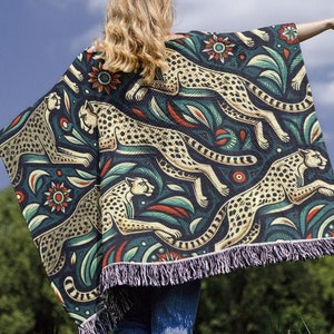 May include: A woman wearing a blue and green patterned throw blanket with a fringe border. The blanket features a repeating design of cheetahs and floral motifs.