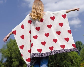 May include: A white poncho with red heart print and fringe trim. The poncho is made of a soft, lightweight fabric and is perfect for layering.