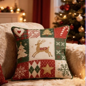 May include: A decorative Christmas pillow with a patchwork design. The pillow features a reindeer, Christmas trees, snowflakes, and a candy cane. The color scheme includes red, green, and white, with a green border. The pillow is on a beige surface.
