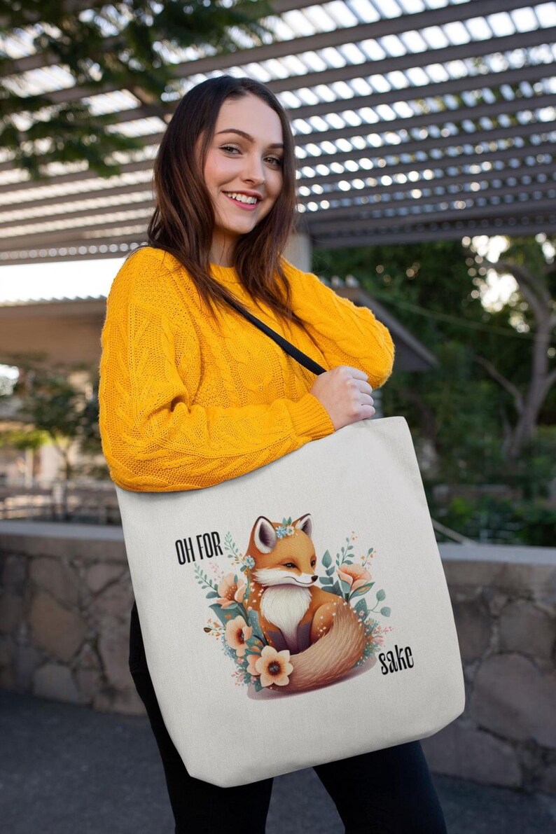 A woman wearing a yellow sweater is holding a white tote bag with a fox graphic and the text "Oh for sah!" printed on it.