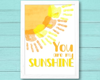 May include: A white framed print featuring a yellow and orange sun created using handprints. The text "You are my sunshine" is written beneath the sun.