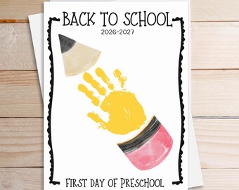 May include: A white rectangular card featuring the text BACK TO SCHOOL 2026-2027 and FIRST DAY OF PRESCHOOL in black. A watercolor illustration of a pencil is formed by a yellow handprint in the center, with a gray tip and pink eraser.