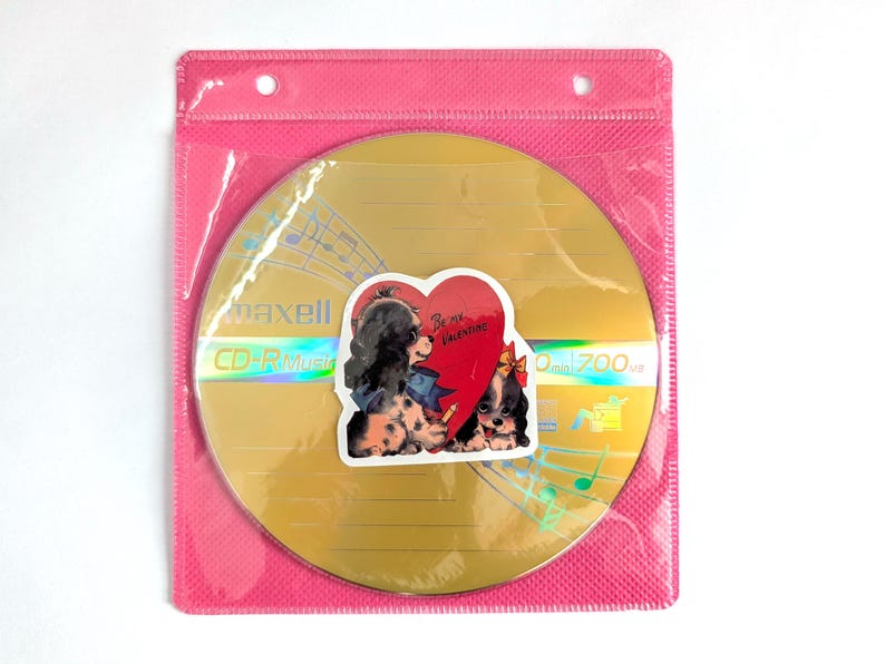 May include: A gold CD-R disc with a sticker featuring two Cavalier King Charles Spaniels and a heart that says "Be my Valentine." The disc is in a pink plastic sleeve. The CD-R has the text "maxell CD-R Music" and "700MB".