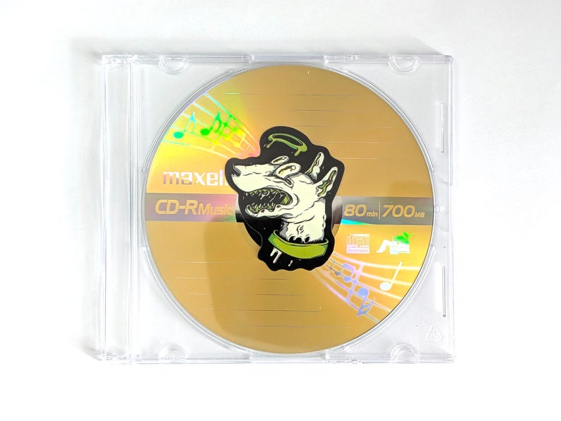 May include: A gold CD-R disc with a cartoon dog graphic in a clear plastic case. The disc has the text "maxell CD-R Music" and "80 min 700MB". Musical notes are also visible.