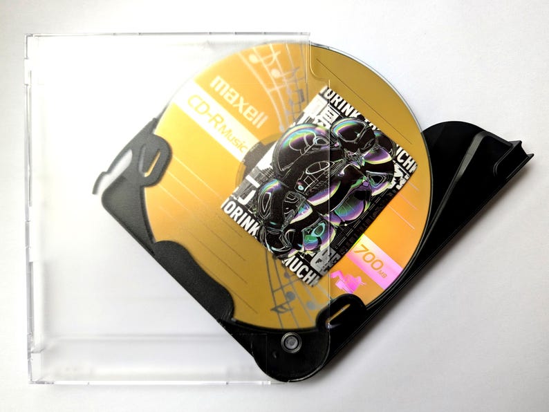 May include: A gold Maxell CD-R Music disc with a black and white graphic design, inside a clear plastic case. The disc has the text "TORINK" and "700MB" printed on it. The case is partially open.
