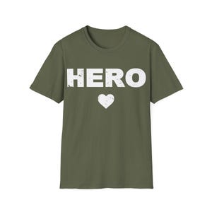 May include: Olive green t-shirt with the word "HERO" in distressed white lettering and a white heart below. The shirt has a crew neck and short sleeves, suitable for casual wear.
