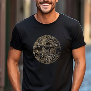 Könnte beinhalten: Schwarzes Rundhals-T-Shirt mit einem goldfarbenen Leiterplattendesign in Kugelform. Das Design ist detailliert und komplex und ähnelt einem Globus. Das Shirt besteht aus einem weichen Material.