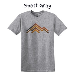 Puede incluir: Camiseta Sport Gray gris claro con un gr&aacute;fico de monta&ntilde;a. El dise&ntilde;o de la monta&ntilde;a presenta l&iacute;neas marrones, naranjas y grises. La camiseta es de color gris claro.