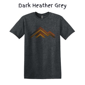 Puede incluir: Camiseta gris jaspeado oscuro con un dise&ntilde;o de monta&ntilde;a en tonos naranja y marr&oacute;n. El texto "Dark Heather Grey" est&aacute; encima de la camiseta. Una camiseta c&oacute;moda para el uso diario.