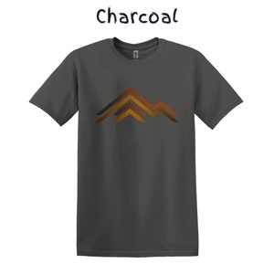Puede incluir: Camiseta de color carb&oacute;n con un dise&ntilde;o de cordillera en tonos naranja, marr&oacute;n y gris. La palabra "Charcoal" est&aacute; escrita en cursiva encima de la camiseta.