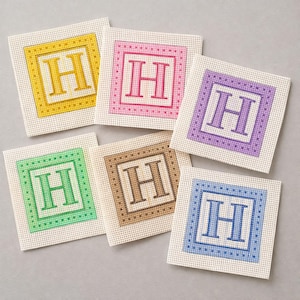 May include: A collection of six square needlepoint coasters, each featuring a different color scheme. The central design is the letter "H" within a square border. Colors include yellow, pink, purple, green, brown, and blue.