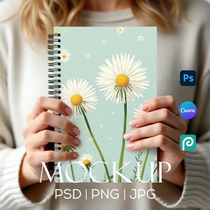 Könnte beinhalten: Ein Spiralblock-Mockup mit einem hellblauen Cover, das weiße Gänseblümchen auf einem hellgrünen Hintergrund zeigt. Der Text "MOCK UP" und "PSD | PNG | JPG" ist unten auf dem Notizblock gedruckt.