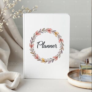 May include: White planner with a floral wreath design and the word "Planner" in black text.