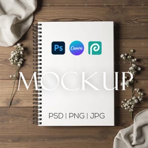 Puede incluir: Maqueta de cuaderno blanco con espiral en una superficie de madera con flores blancas y tela. El cuaderno tiene el texto "MOCKUP" y "PSD | PNG | JPG" impreso en él. El cuaderno también tiene tres logotipos: "Ps", "Canva" y un círculo azul y verde con una "P" dentro.
