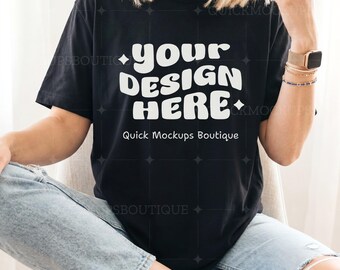 May include: Black t-shirt with the text "your DESIGN HERE" in a white, retro font. The shirt also features the text "Quick Mockups Boutique" in a smaller font. The model is wearing light blue jeans and white sneakers.