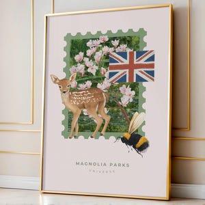 Op de afbeelding: Een ingelijste kunstprint met een hertje, magnoliabloesems, een Britse vlag en een hommel, geplaatst in een groen postzegelontwerp. De tekst "MAGNOLIA PARKS UNIVERSE" staat onderaan. Het kunstwerk is in een gouden lijst.