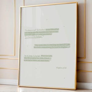 May include: A framed print with a gold frame, featuring text excerpts from a book. The text is in a light green font on a white background. The words "Kingdom of Ash" are at the bottom.