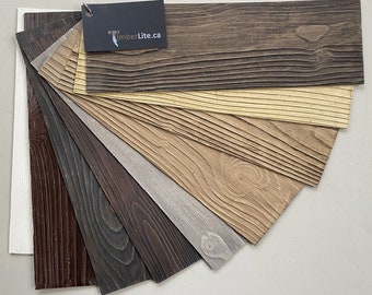 May include: A fan-shaped display of eight wood-look wall panel samples in various shades of brown, gray, and beige. The panels have a wood grain texture and are arranged in a gradient from dark to light. The TimberLite.ca logo is visible on a black tag.