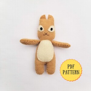 May include: A brown felt bunny with white felt accents. The bunny has black eyes and a stitched smile. The image includes the text "PDF PATTERN".