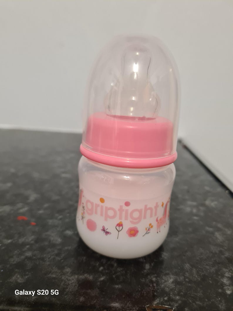 Peut inclure: Un biberon rose pour b&eacute;b&eacute; avec un couvercle transparent et une &eacute;tiquette blanche sur laquelle est inscrit "griptight" avec un motif de papillon et de fleurs.