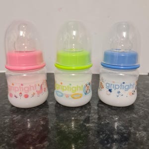 Peut inclure: Trois biberons pour b&eacute;b&eacute;s avec des couvercles et des motifs de couleurs diff&eacute;rentes. Les biberons sont &eacute;tiquet&eacute;s "griptight" et pr&eacute;sentent une licorne, un flotteur de piscine et un ballon de football.