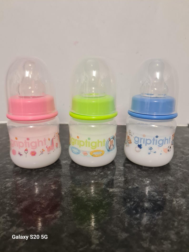 Peut inclure: Trois biberons pour b&eacute;b&eacute;s avec des couvercles et des motifs de couleurs diff&eacute;rentes. Les biberons sont &eacute;tiquet&eacute;s "griptight" et pr&eacute;sentent une licorne, un flotteur de piscine et un ballon de football.