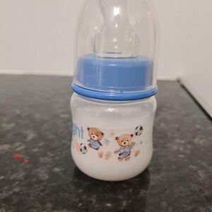 Peut inclure: Un biberon transparent avec un couvercle bleu et un motif bleu et blanc repr&eacute;sentant deux ours en peluche jouant au football. Le biberon a une t&eacute;tine en silicone transparente.